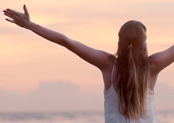 Girl standing with arms raised looking towards sunrise